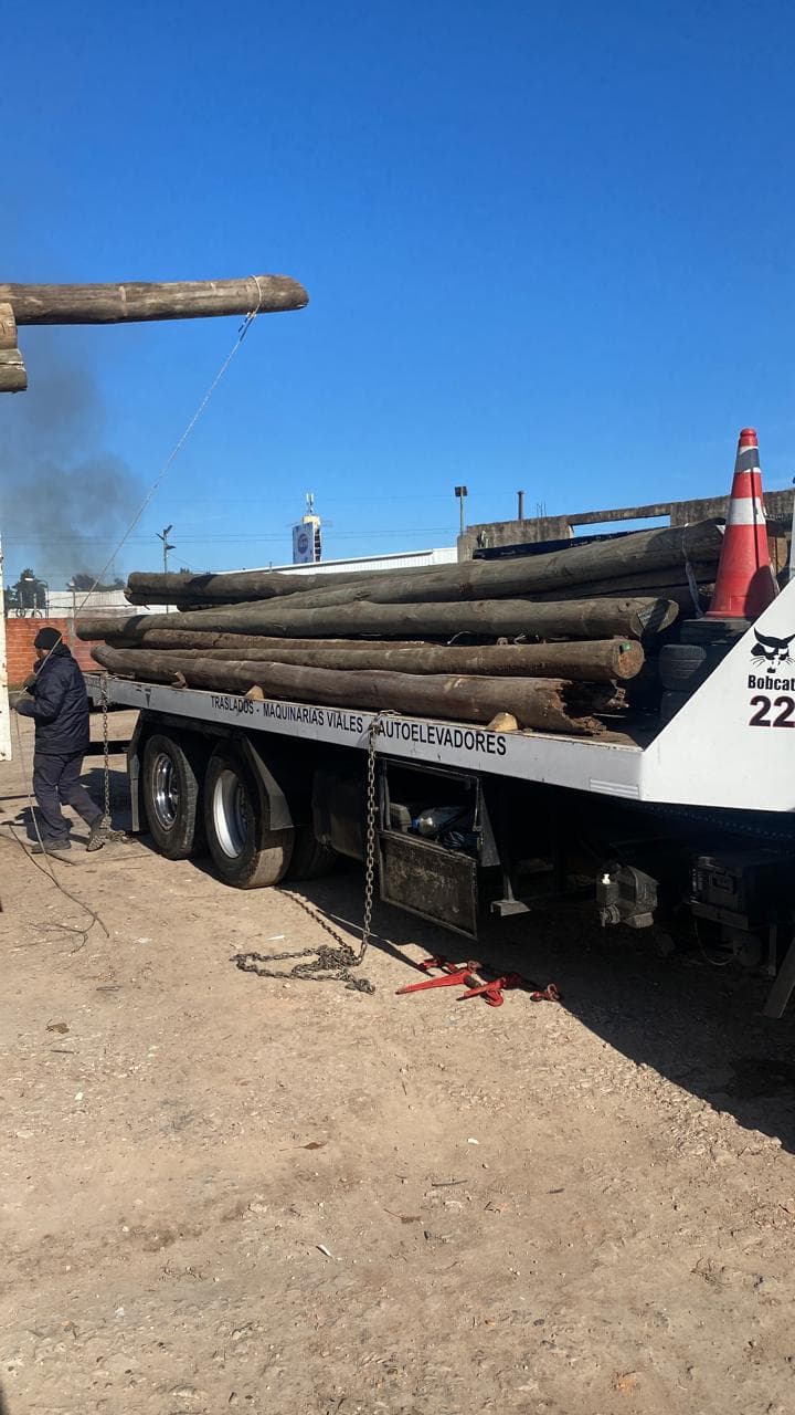 Camión con plataforma cargado de postes de madera, con un operario asegurando la carga